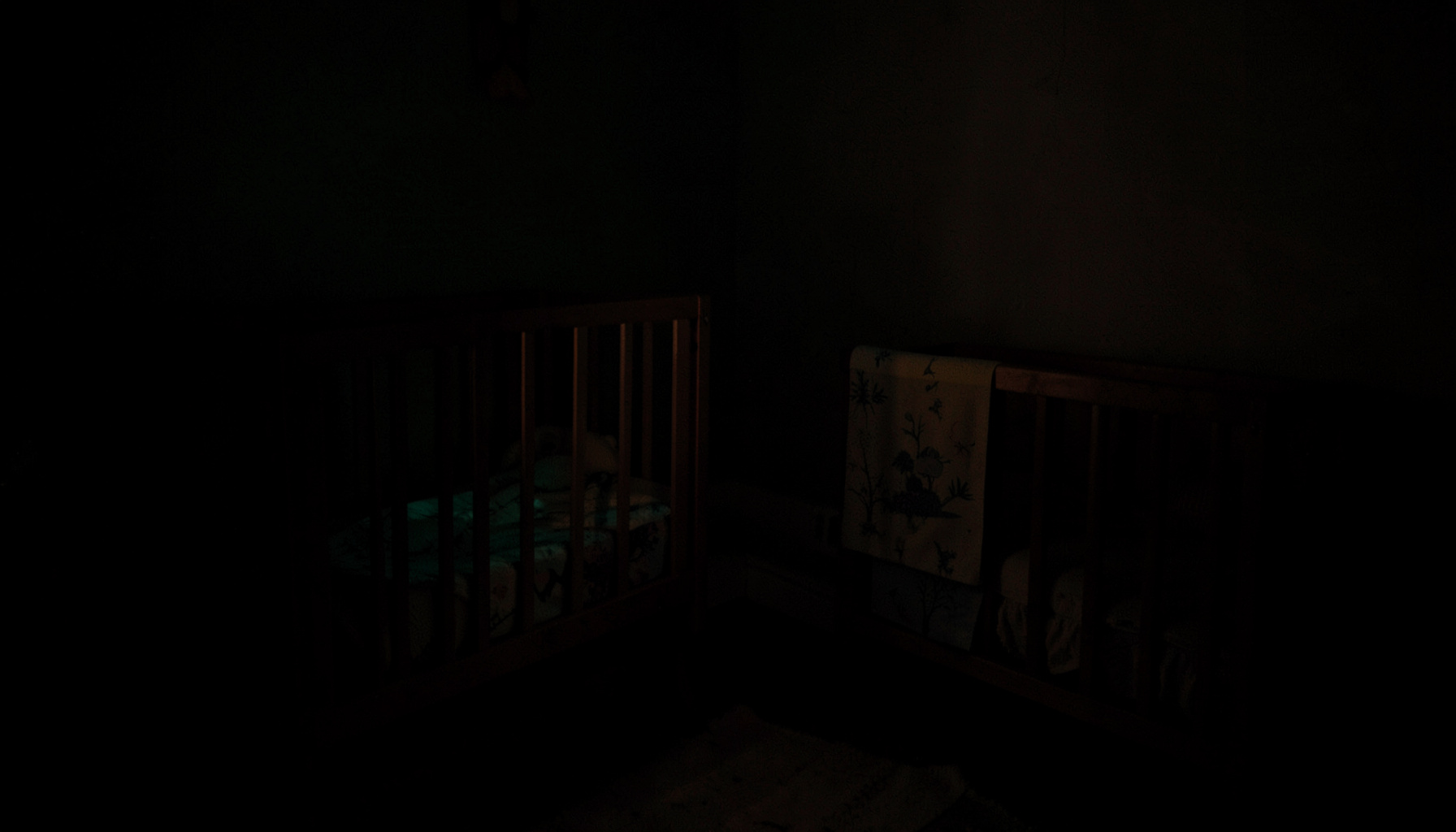 Dark, low-key photograph of a softly lit nursery corner at night, deep shadows with a warm amber glow, quiet and intimate mood